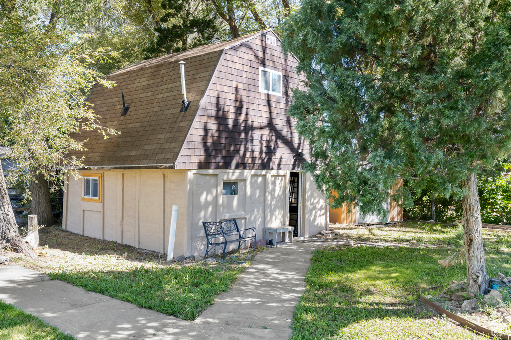 View of front of home with a gambrel roof, a barn, an outdoor structure, roof with shingles, and a front lawn