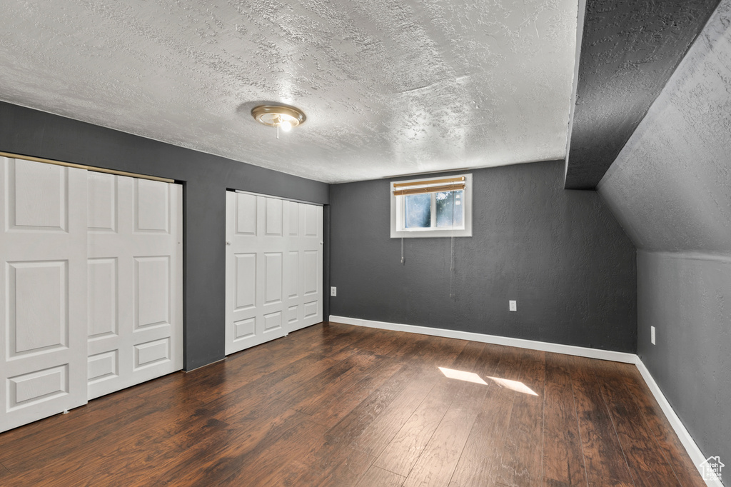 Unfurnished bedroom featuring wood finished floors, a textured ceiling, multiple closets, and lofted ceiling