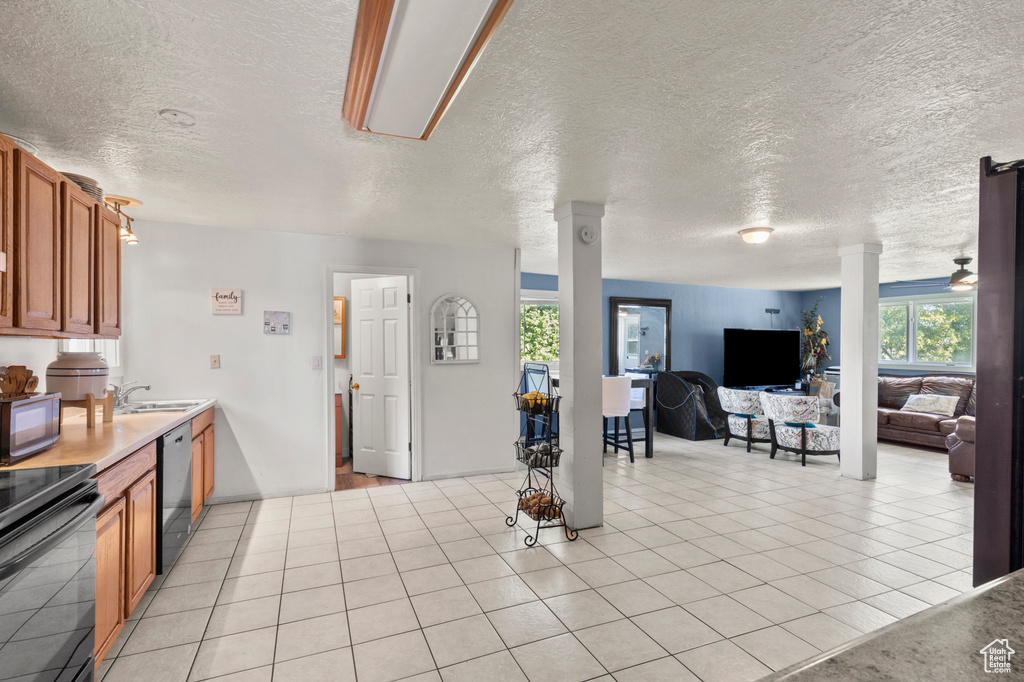 Kitchen featuring black appliances, a textured ceiling, brown cabinets, open floor plan, and ornate columns