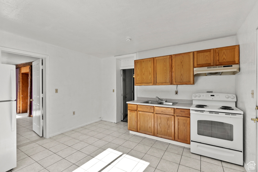 Kitchen featuring white appliances, under cabinet range hood, light countertops, light tile patterned floors, and brown cabinets