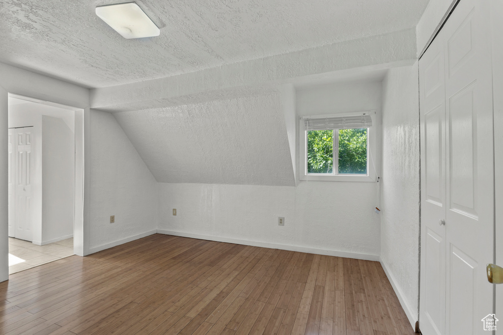 Bonus room with wood-type flooring, a textured ceiling, and vaulted ceiling
