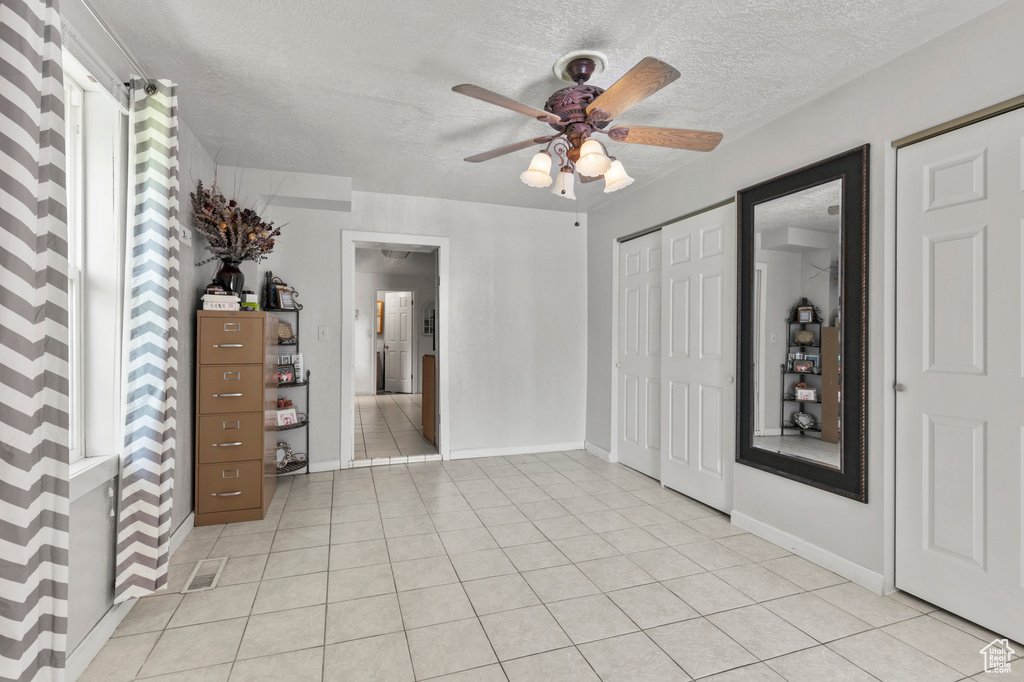Unfurnished bedroom featuring a textured ceiling, light tile patterned floors, and ceiling fan