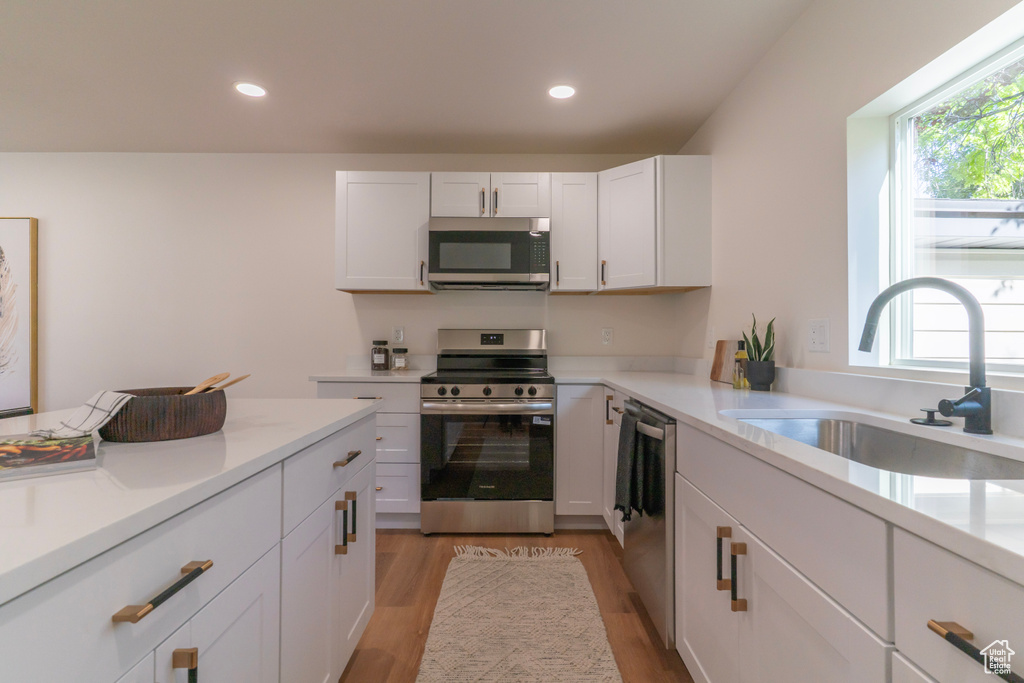 Kitchen with stainless steel appliances, light wood-style floors, white cabinets, light countertops, and recessed lighting
