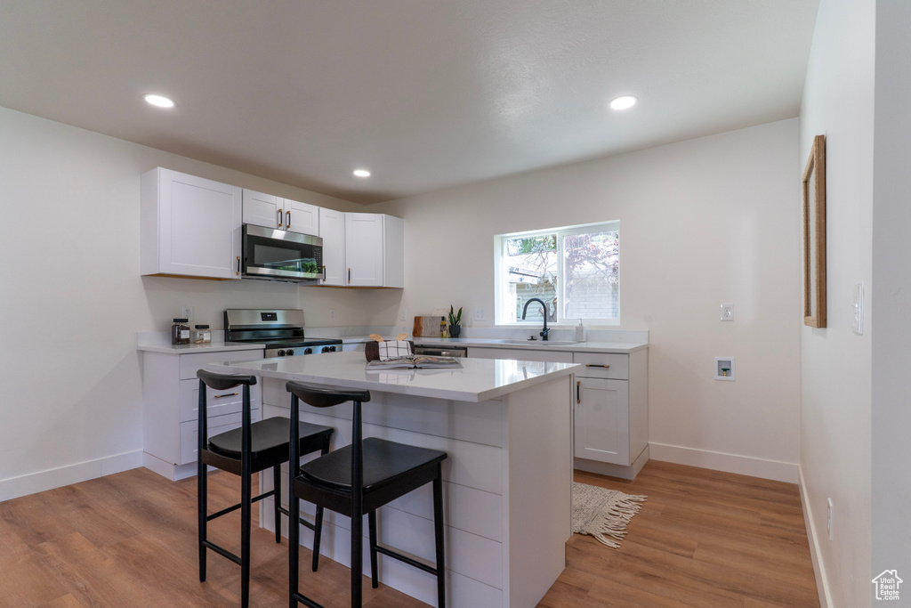 Kitchen with stainless steel appliances, a breakfast bar, light countertops, white cabinetry, and light wood-style floors