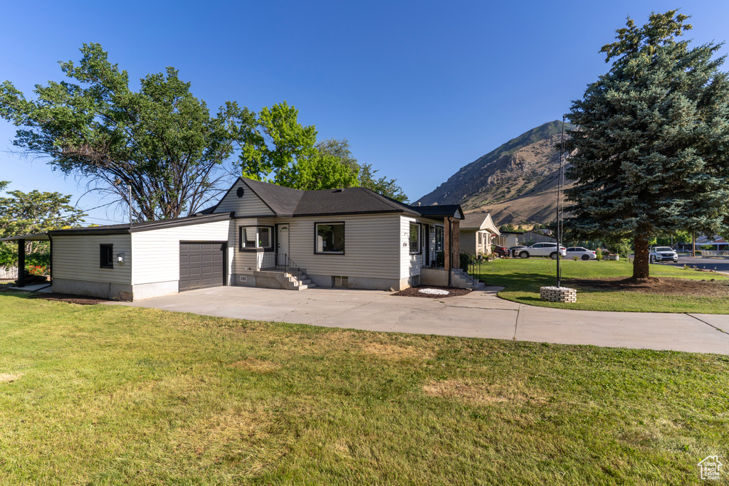 View of front of house with a garage, driveway, a front lawn, and a mountain view