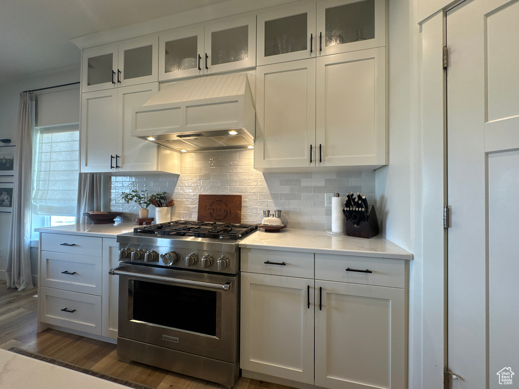 Kitchen with high end range, custom range hood, white cabinetry, backsplash, and dark wood-type flooring
