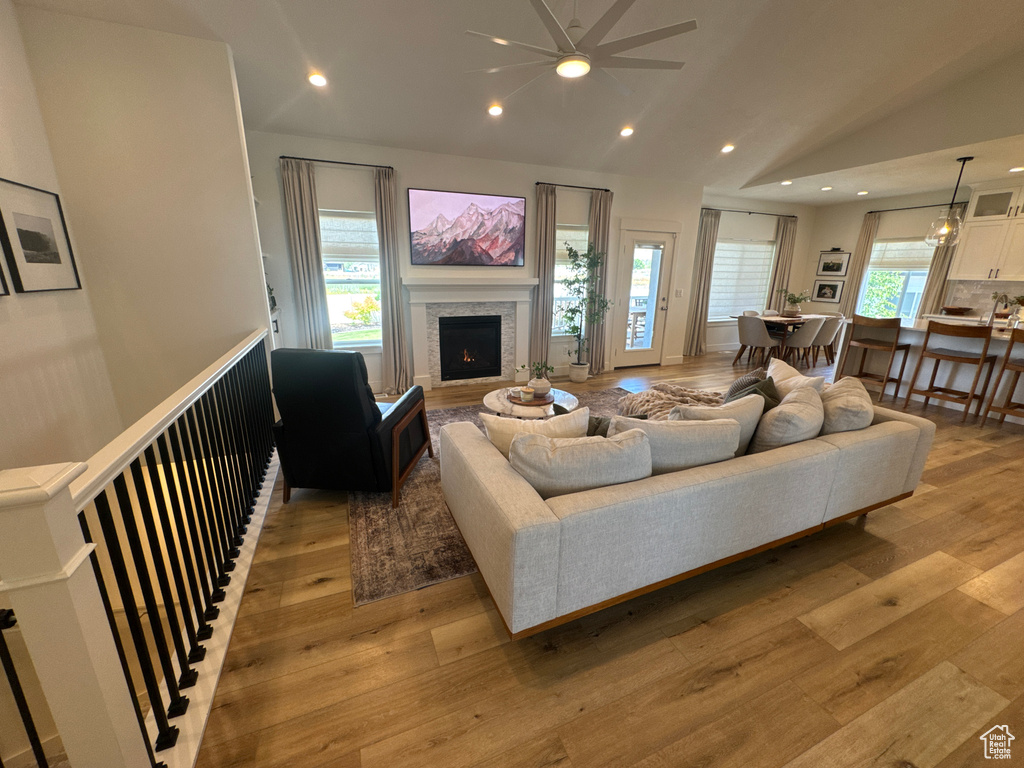 Living area featuring lofted ceiling, light wood-style floors, a lit fireplace, recessed lighting, and a ceiling fan