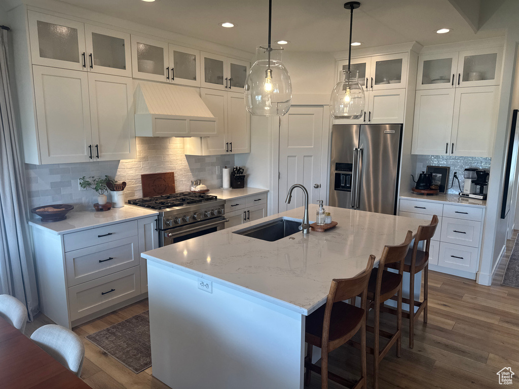 Kitchen with high quality appliances, custom exhaust hood, dark wood-style flooring, decorative backsplash, and white cabinets