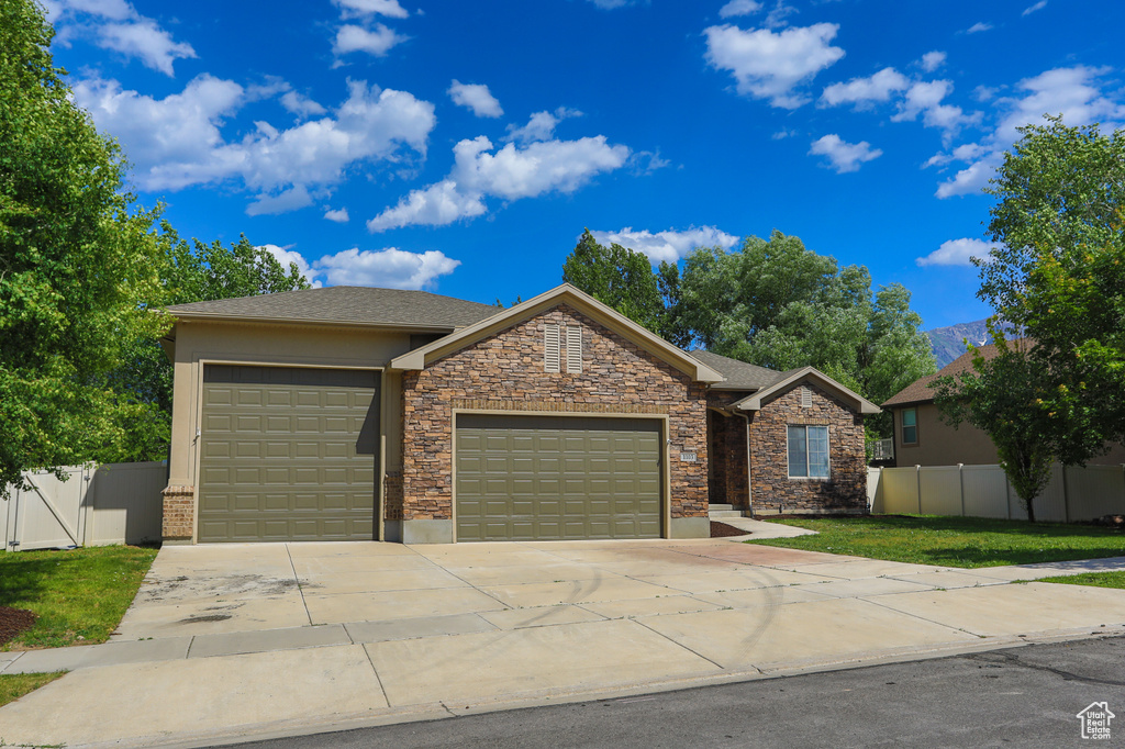 View of front facade with an attached garage, driveway, stucco siding, and stone siding
