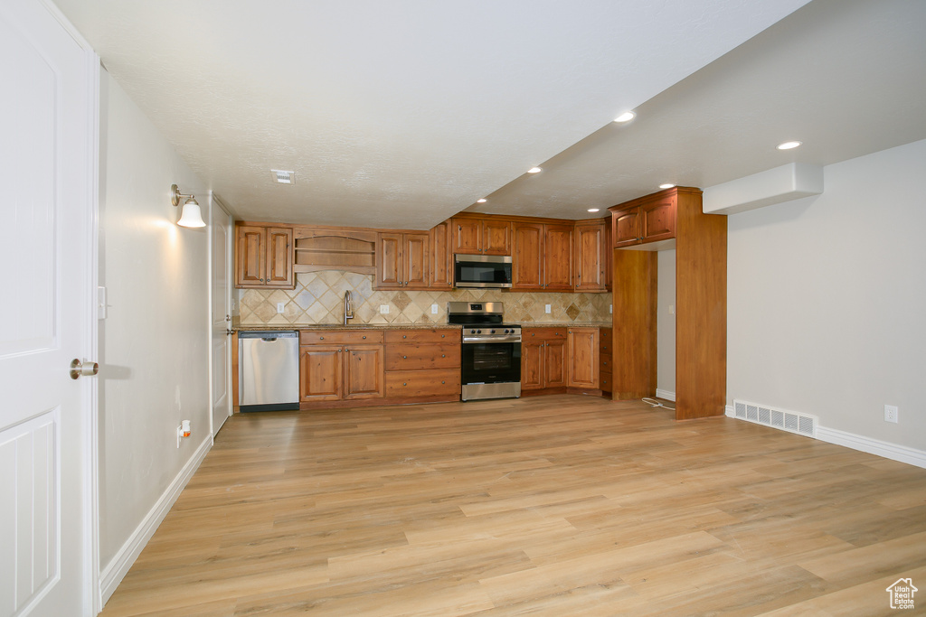 Kitchen featuring stainless steel appliances, tasteful backsplash, recessed lighting, light wood finished floors, and brown cabinetry