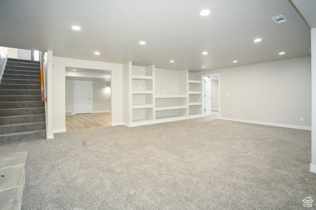 Unfurnished living room with light colored carpet, recessed lighting, and stairs