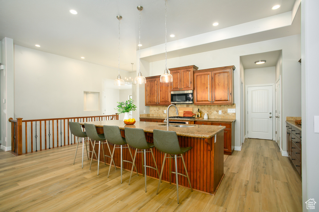 Kitchen featuring stainless steel microwave, light wood finished floors, a breakfast bar area, a center island with sink, and brown cabinetry
