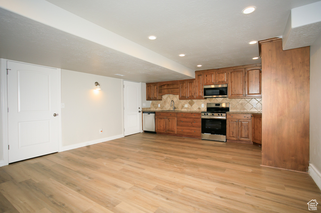 Kitchen with stainless steel appliances, brown cabinetry, decorative backsplash, light wood-style flooring, and light countertops