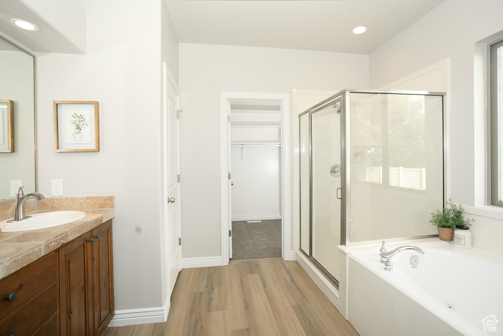 Full bath featuring a shower stall, wood finished floors, vanity, a bath, and a walk in closet