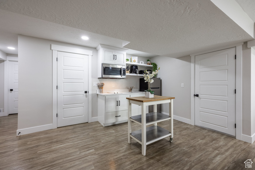 Kitchen featuring stainless steel appliances, open shelves, wood finished floors, white cabinets, and a textured ceiling