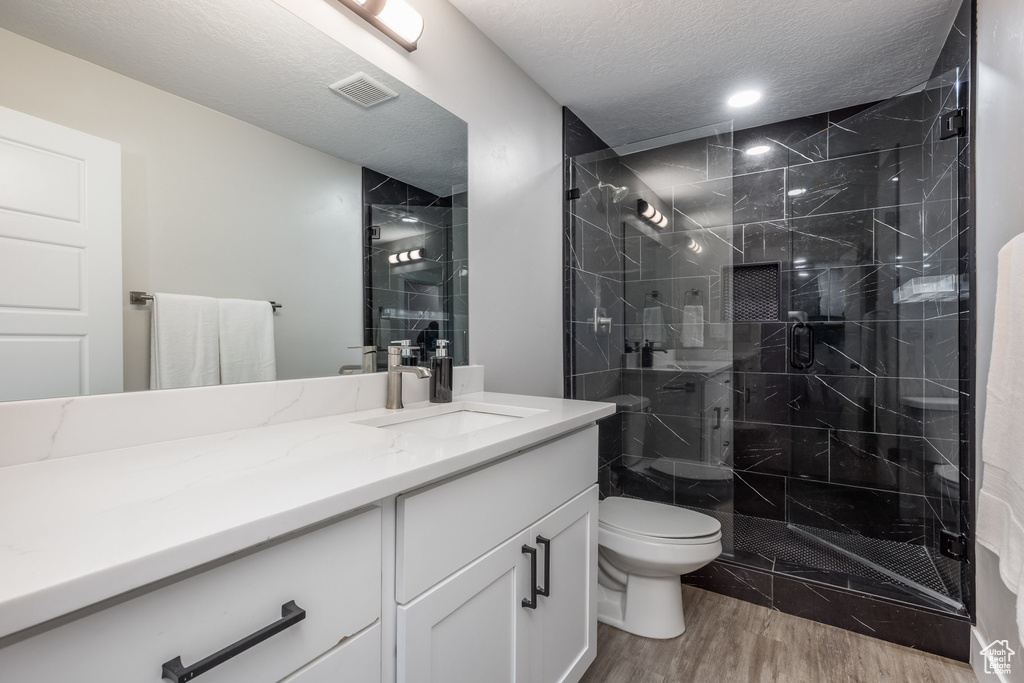 Full bath featuring wood finished floors, vanity, a stall shower, and a textured ceiling