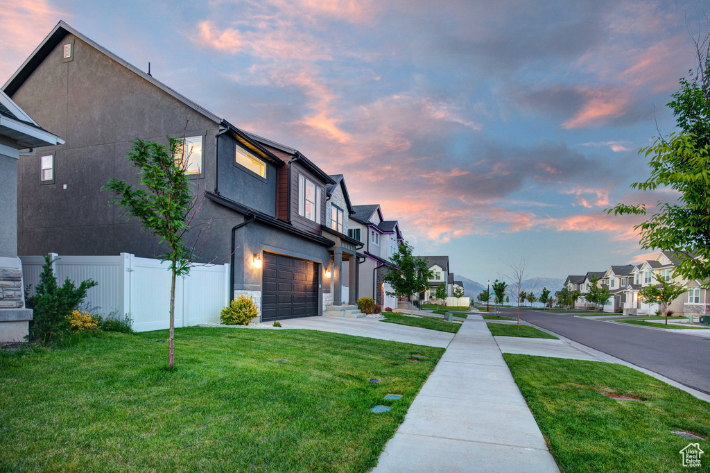 Property exterior at dusk featuring a garage, a residential view, driveway, stone siding, and stucco siding
