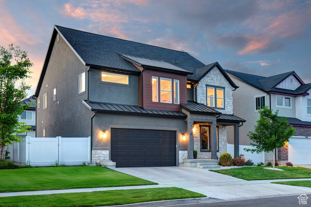 View of front of property with a standing seam roof, stone siding, an attached garage, driveway, and roof with shingles