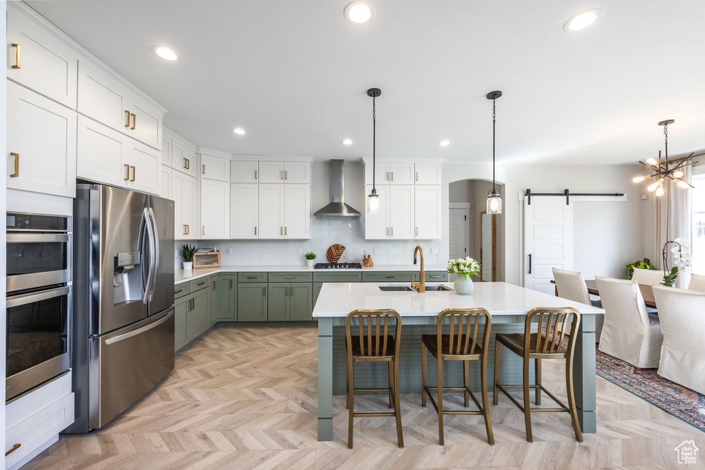 Kitchen featuring stainless steel appliances, wall chimney exhaust hood, a barn door, white cabinetry, and recessed lighting