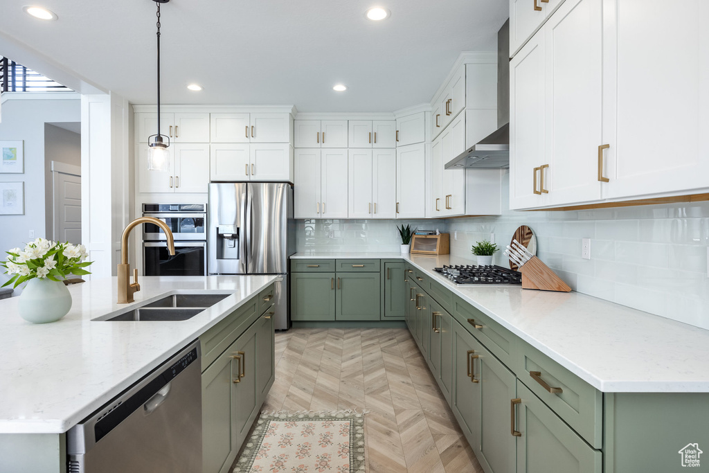 Kitchen featuring appliances with stainless steel finishes, green cabinetry, white cabinets, recessed lighting, and wall chimney exhaust hood