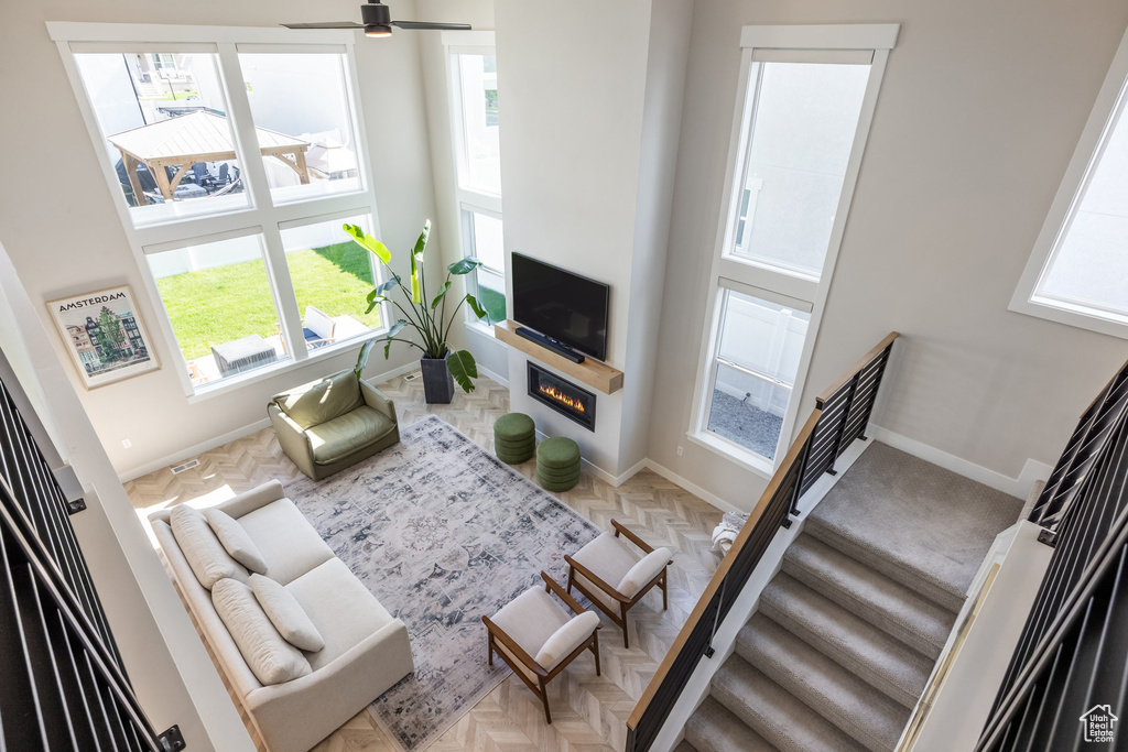 Living area featuring a glass covered fireplace, stairway, and a ceiling fan