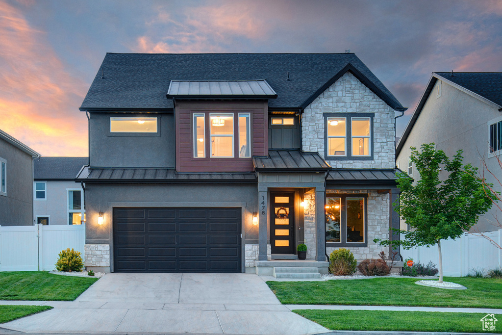 View of front of property featuring a standing seam roof, stone siding, driveway, and a garage