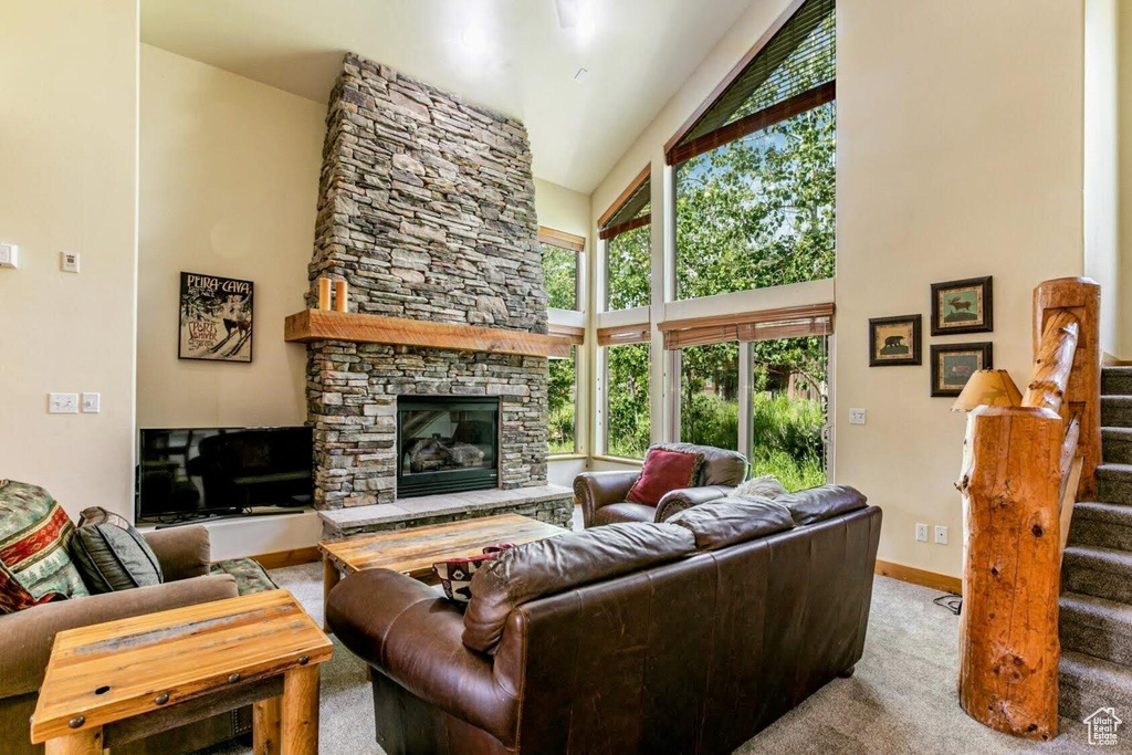 Living area featuring high vaulted ceiling, a stone fireplace, stairway, and carpet flooring