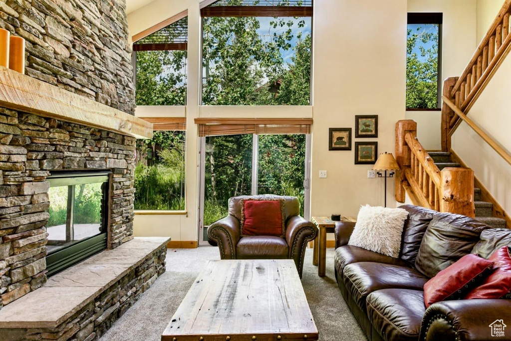 Carpeted living room featuring a high ceiling, stairs, and a stone fireplace