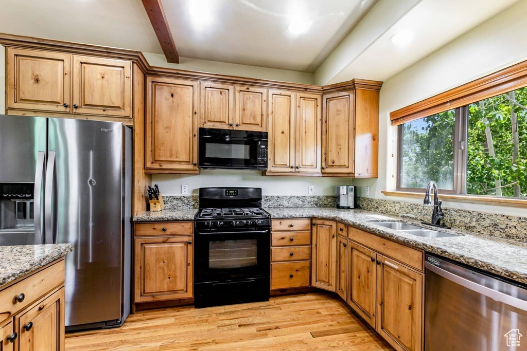 Kitchen featuring black appliances, light wood-style flooring, light stone counters, and beam ceiling