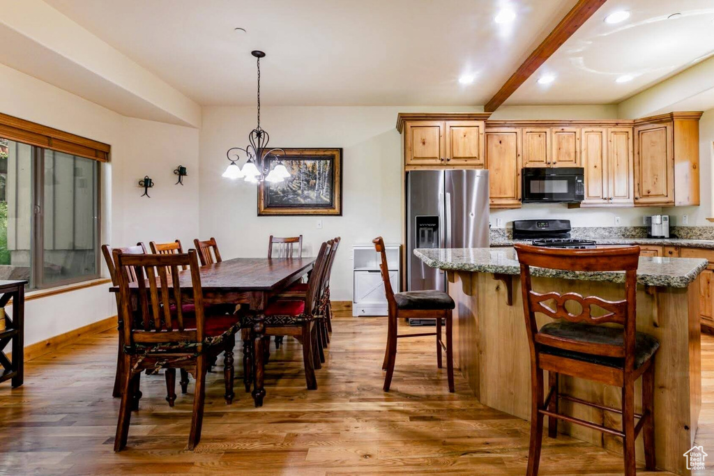 Kitchen with black microwave, stove, stainless steel refrigerator with ice dispenser, wood finished floors, and a center island