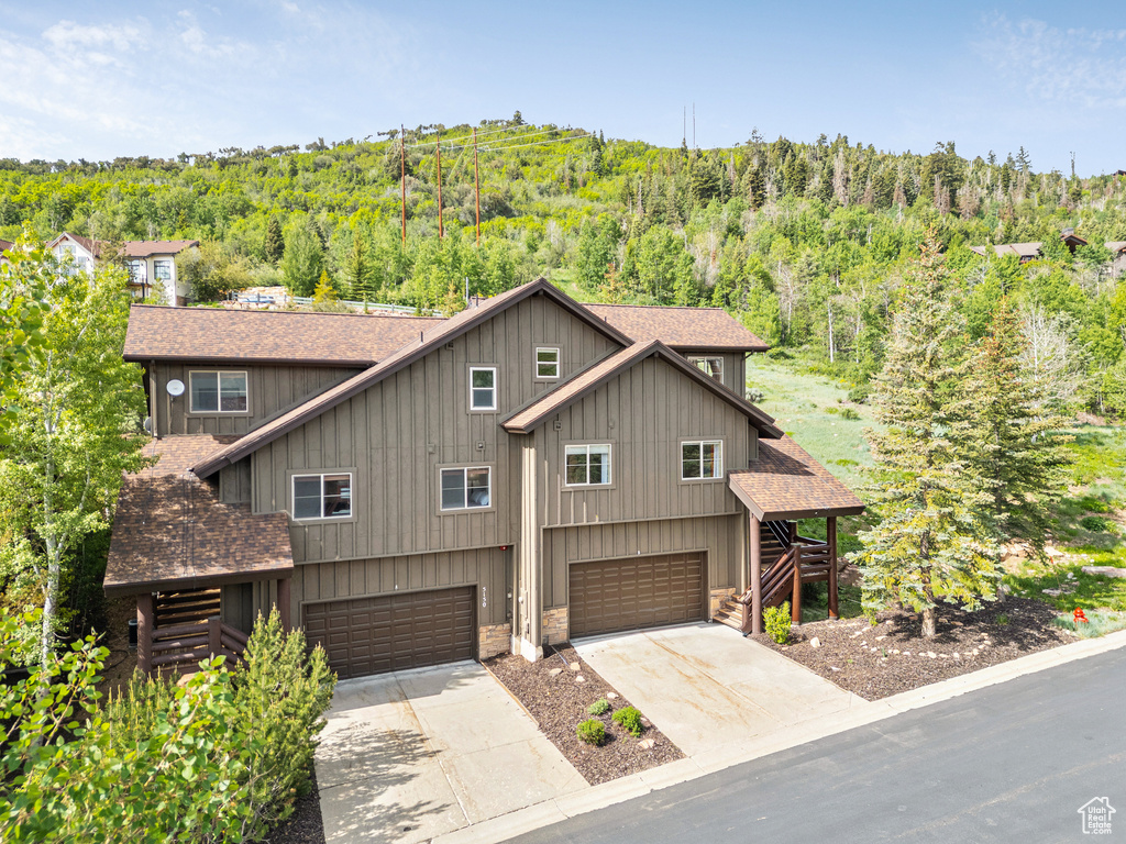 View of front of home featuring a shingled roof, a view of trees, a garage, stairway, and concrete driveway