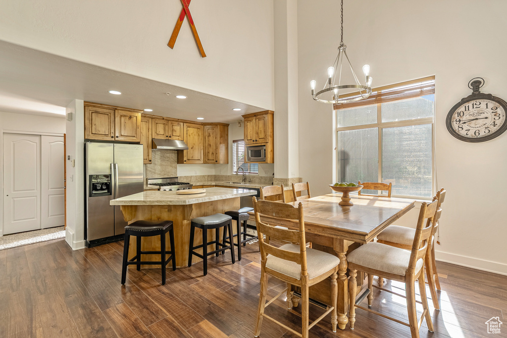 Dining space with a chandelier, plenty of natural light, a high ceiling, dark wood-style floors, and recessed lighting