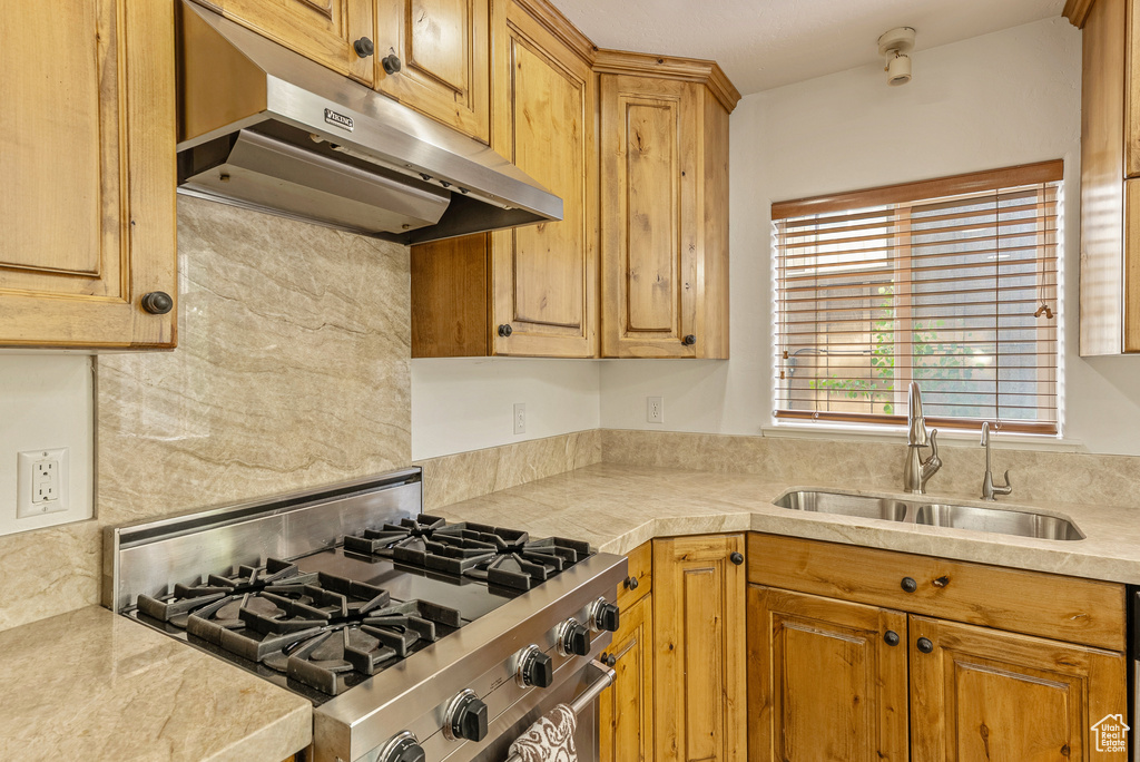 Kitchen featuring stove, under cabinet range hood, light countertops, and decorative backsplash