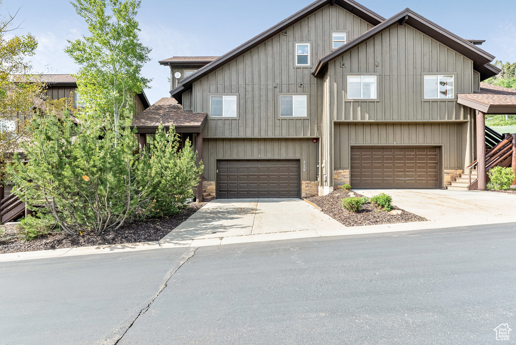 View of front facade with roof with shingles, stone siding, an attached garage, and driveway