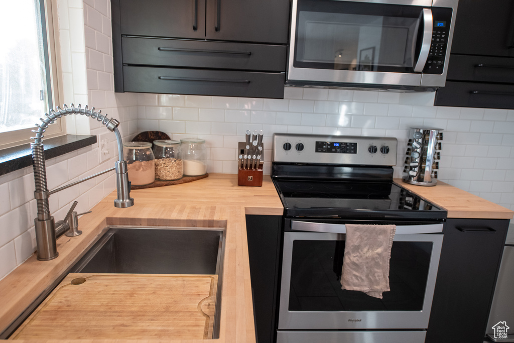 Kitchen featuring appliances with stainless steel finishes, wood counters, backsplash, and dark cabinetry