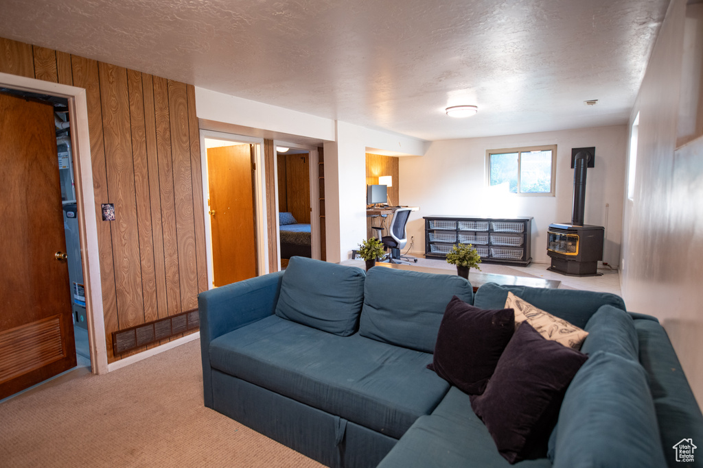 Living room with a wood stove, wooden walls, carpet, and a textured ceiling