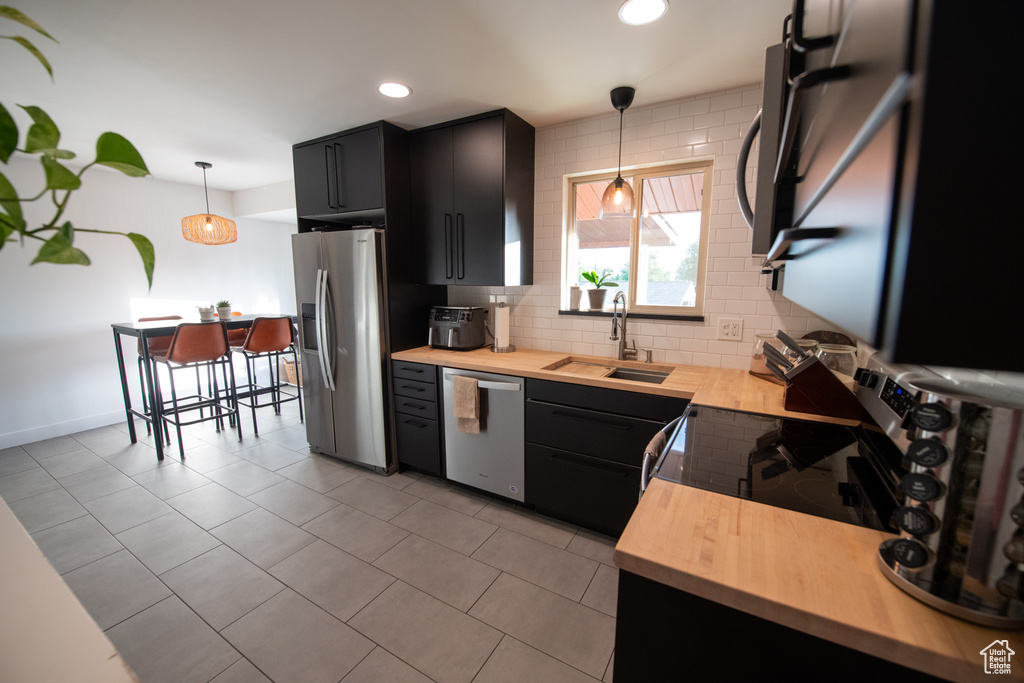 Kitchen featuring appliances with stainless steel finishes, wooden counters, dark cabinets, decorative backsplash, and decorative light fixtures