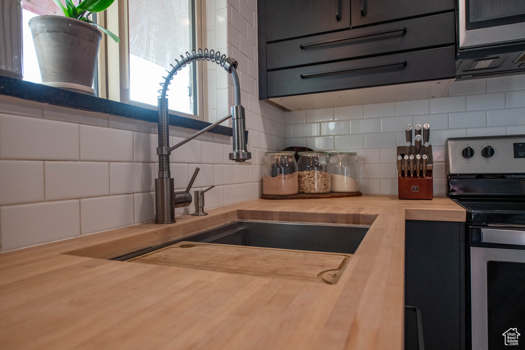 Kitchen with butcher block counters, stainless steel appliances, tasteful backsplash, and dark cabinets