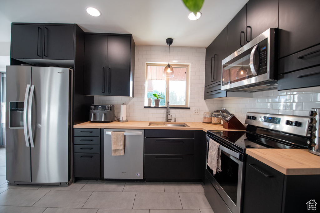 Kitchen featuring appliances with stainless steel finishes, butcher block counters, dark cabinetry, backsplash, and light tile patterned floors