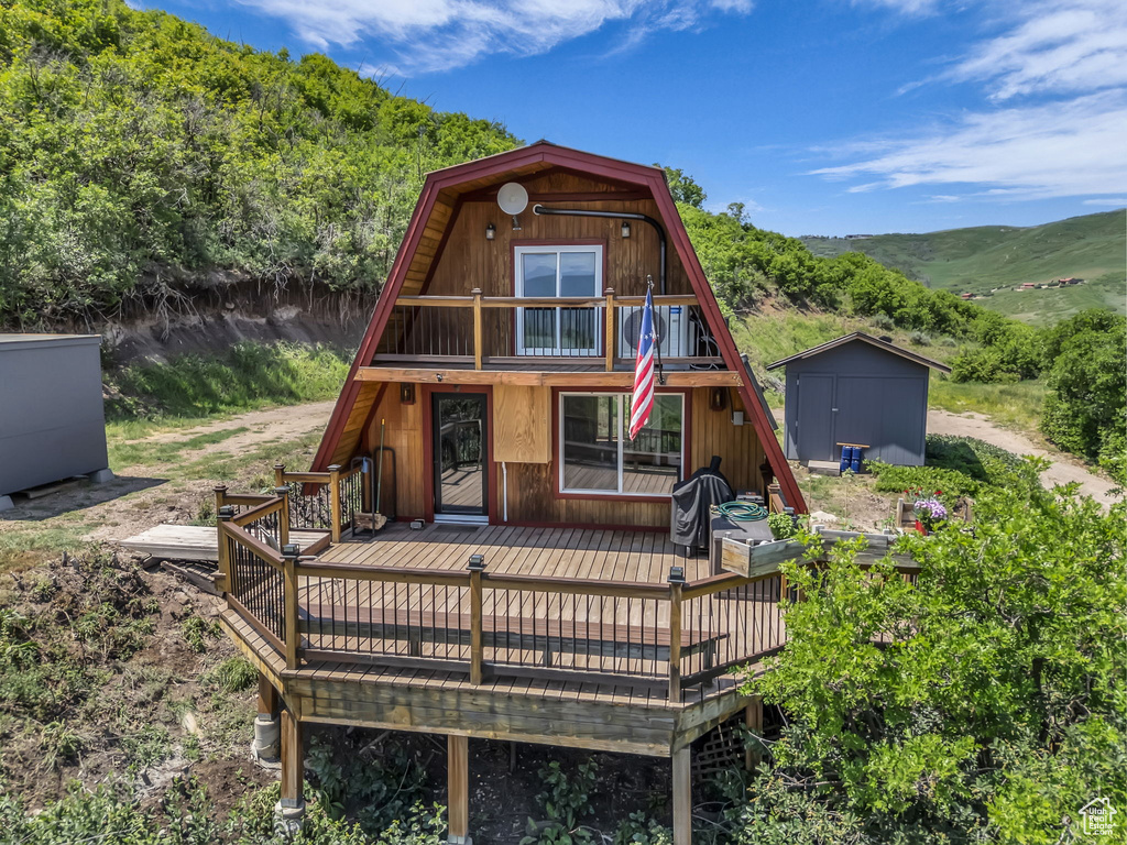 Rear view of property with a storage unit, a deck with mountain view, and a gambrel roof