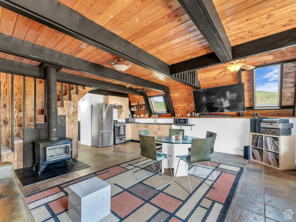 Dining room featuring stone tile floors, a wood stove, healthy amount of natural light, wood walls, and a wooden ceiling with exposed beams