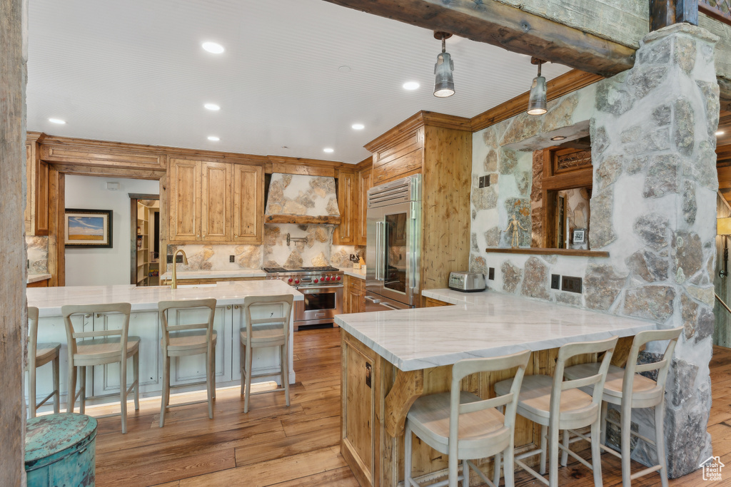 Kitchen with custom range hood, stainless steel appliances, light wood-type flooring, decorative backsplash, and light stone counters