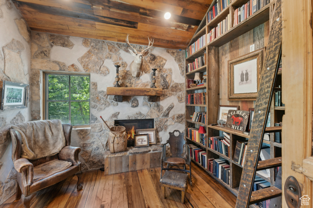 Living area with hardwood / wood-style flooring, a stone fireplace, and a wooden ceiling with exposed beams
