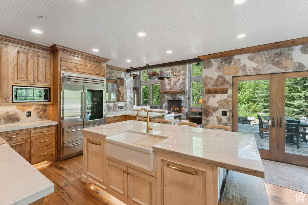 Kitchen with built in appliances, a fireplace, french doors, light wood finished floors, and light stone countertops