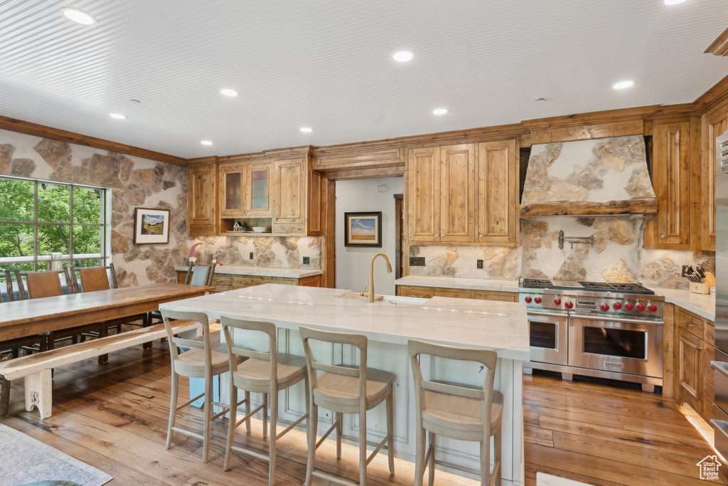 Kitchen featuring custom range hood, range with two ovens, tasteful backsplash, light wood-type flooring, and recessed lighting
