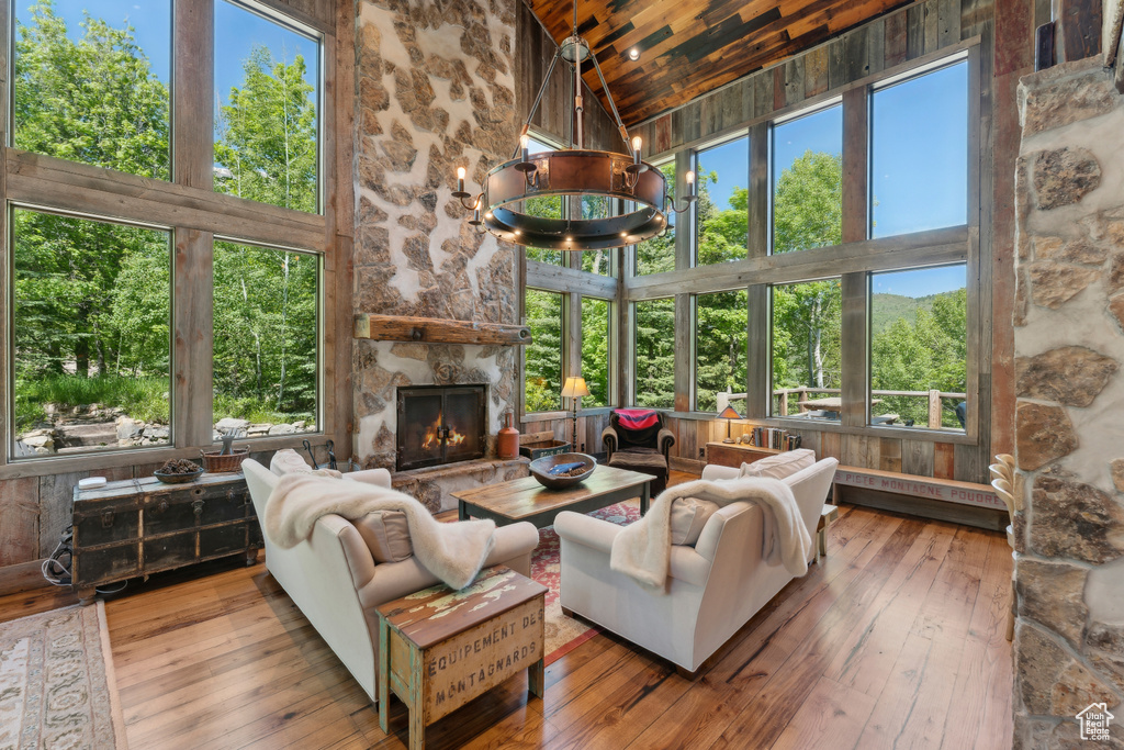 Living area featuring high vaulted ceiling, wooden ceiling, hardwood / wood-style floors, a chandelier, and a stone fireplace
