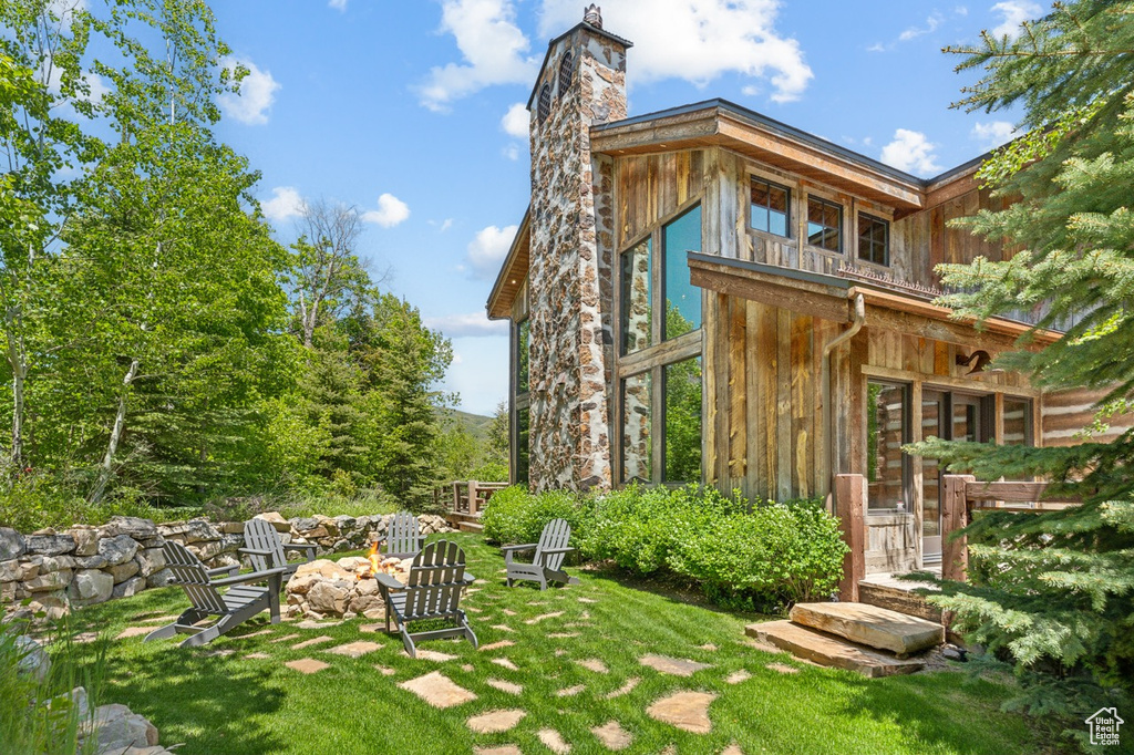 Rear view of house with a fire pit, a chimney, a lawn, and board and batten siding