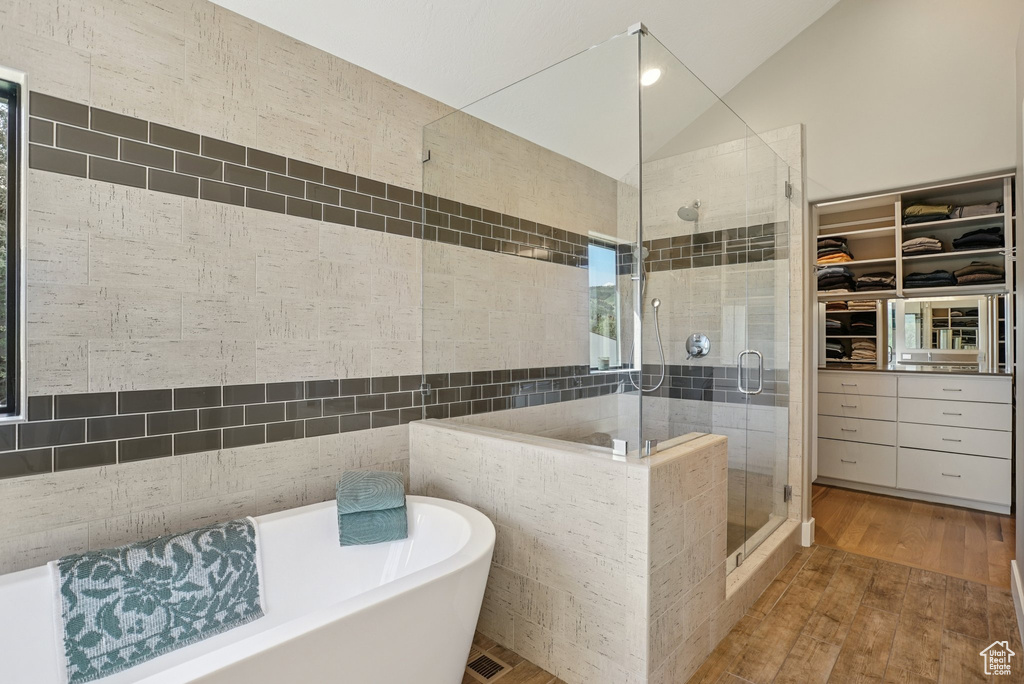 Full bathroom featuring a shower stall, wood finished floors, a soaking tub, a walk in closet, and lofted ceiling