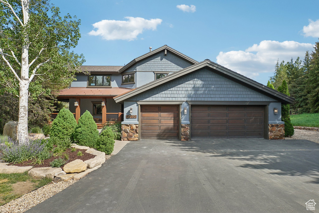 View of front facade featuring driveway, stone siding, and an attached garage