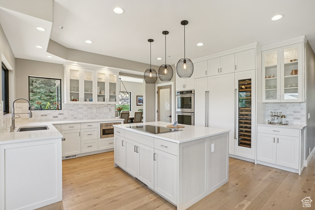 Kitchen with stainless steel double oven, black electric stovetop, decorative backsplash, recessed lighting, and a kitchen island